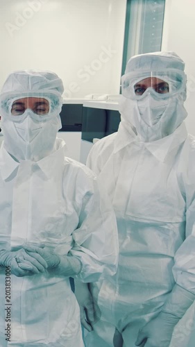 Two researchers in a cleanroom, wearing full protective gear. They stand in a medical laboratory setting. Ideal for stock imagery related to biotechnology and safety protocols.