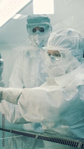 In a sterile cleanroom, two dedicated scientists, indistinguishable in gender or ethnicity due to their full protective suits, meticulously work in a medical laboratory.