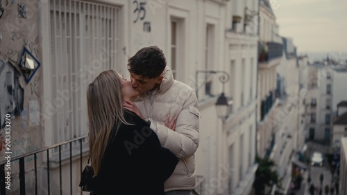 A young couple kisses romantically on a street in Montmartre Paris France The image showcases love and affection in an urban setting with old buildings and graffiti suitable for travel and lifestyle c