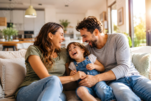 A happy family of three sitting on a couch in a modern living room laughing and enjoying quality time together