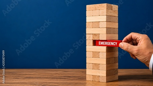 Hand pulling red emergency wooden block from jenga tower stack on blue background, business risk crisis management with strategic decision making in conceptual composition
