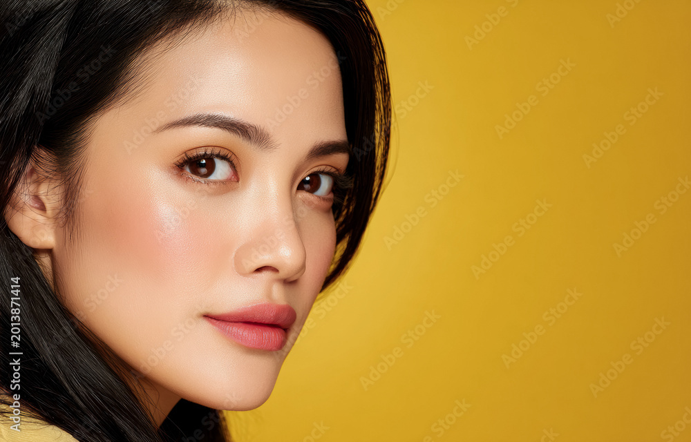 Naklejka premium Stylish Asian female model poses with modern makeup and smooth skin. Bright yellow tones create a bold fashion beauty portrait scene.