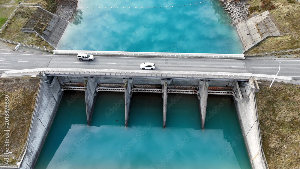 Fototapeta premium Aerial View of Cars Crossing Lake Tekapo Dam Bridge in New Zealand
