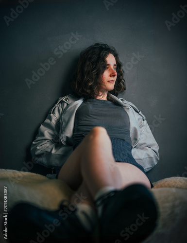 Beautiful young girl with beautiful legs sitting casually, lost in thought while wearing a simple top, shorts, and a leather jacket, in an intimate and moody setting