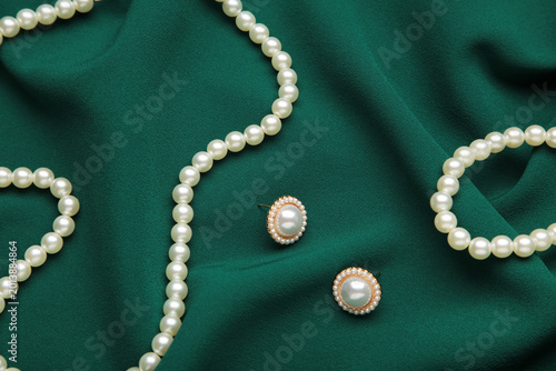 Beautiful pearl bracelet, earring, and necklace on green texture background