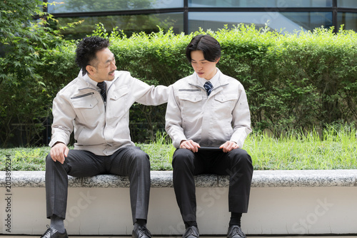 休憩中に会話する作業員のポートレート職場の人間関係性、上司が励ます落ち込む悩む部下、信頼イメージ全身　5月病の部下の話を聞く上司