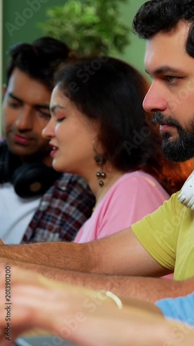 Indian college students using laptop to complete assignment with books, notes, preparing for exams studying in a focused, collaborative environment inside a university campus library in exam season