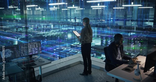 Technology Specialists Activate Information Flows in a Futuristic Data Center, Monitoring Servers, AI Analytics, Cloud Systems, Network Visualization Across Digital Infrastructure. Elevated Shot