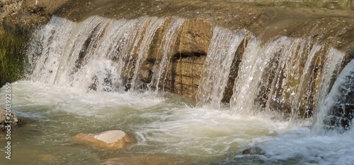 Small natural waterfall flowing through rocky stream in forest landscape
