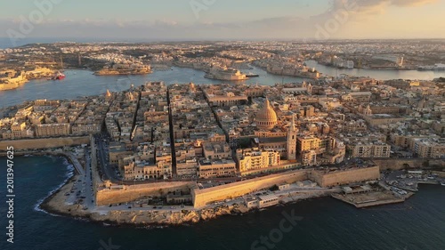 Aerial of defensive stone walls protecting coastal peninsula of Valletta, Malta. Sunset light illuminates historic buildings of Valletta, Malta. Mediterranean sea borders the harbor of Valletta