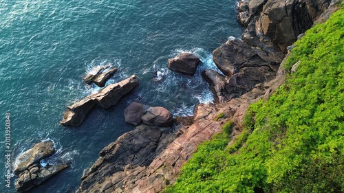 Aerial view of turquoise ocean waves crashing against rocky coastline during soft morning light. Calm yet powerful seascape with natural textures of water and cliffs.