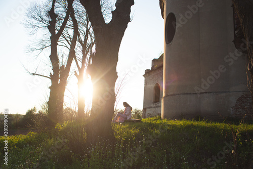 Fotografi Young woman sitting by the ruins of Mary Magdalene Church during a bright sunset