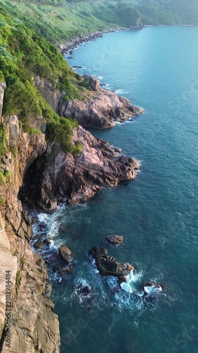 Drone view of powerful waves crashing on rocky shore at sunrise. Scenic tropical coastline with calm morning atmosphere and turquoise water