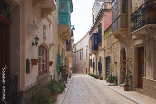 Scenic narrow street in Mdina with traditional colorful Maltese balconies
