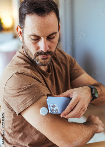 Man Checking Continuous Glucose Monitor With Smartphone App While Sitting Indoors, Health Technology Moment