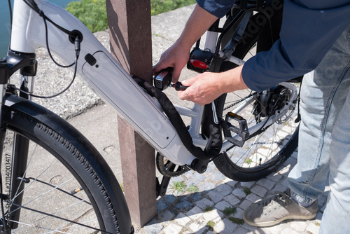 Young man in helmet securing his electric bicycle with a lock at a city bike rack near the water
