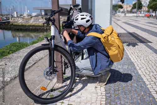 Fotografie Young man in helmet securing his electric bicycle with a lock at a city bike rac
