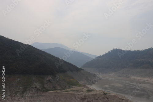Fotografie Dry Reservoir and Exposed Riverbed Between Misty Mountains at Low Water in Uttra