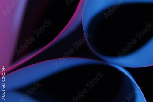 Cuadro en lienzo Papeles de oficina doblados en curvas fluidas, iluminados con luces multicolores en tonos azul, magenta y rojo sobre un fondo negro profundo