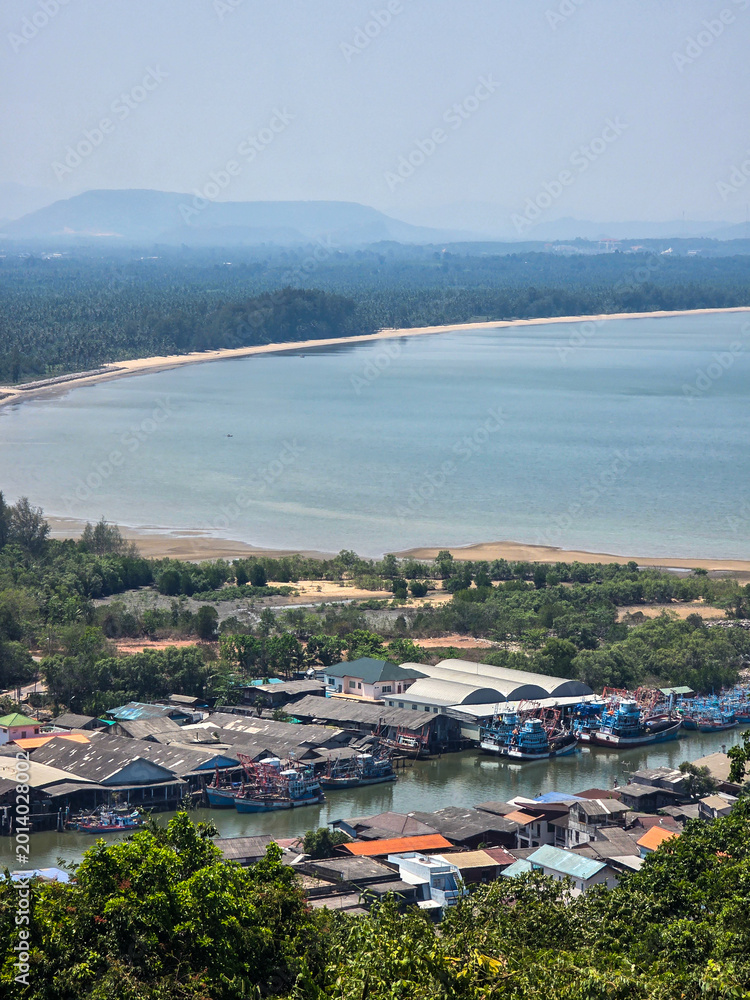 Fototapeta premium Scenic coastal village landscape view showing peaceful ocean bay fishing boats moored at calm harbor under clear sky with distant misty mountain backdrop creating serene tranquil atmosphere