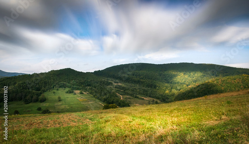 Rolling green hills and forest landscape under dramatic cloudy sky