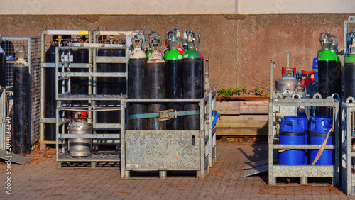 Industrial gas cylinders and oxygen tanks stored in metal crates outdoors. Compressed gas bottles for welding and medical use at a warehouse. Logistics and safety of hazardous materials.