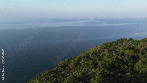 Aerial view of mountains, forest, ocean and a distant city skyline. Tropical landscape with natural and urban contrast.