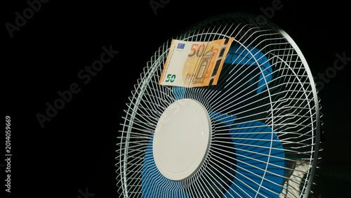 Fotografía Euro banknote caught in electric fan symbolizing money loss during summer heat d