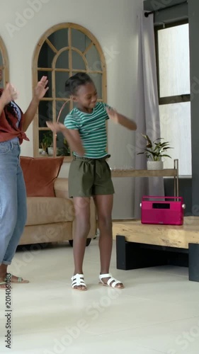 Vertical video: Dancing youth in green top doing quick steps at home to pink radio while mom copies