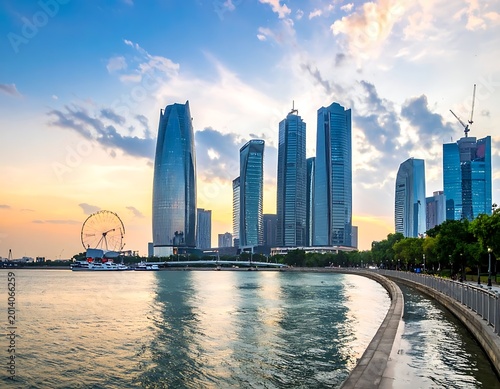 Modern city skyline at sunset. Tall, glass skyscrapers rise over a body of water with a Ferris wheel. A scenic promenade lines the shore