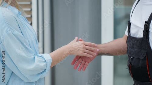 Close-up of a female client signing a contract on a clipboard for a completed job and shaking hands with a male technician in uniform, symbolizing a successful service agreement