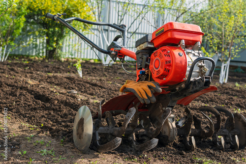 Obraz na plátně Gasoline motor cultivator with protective gloves in the garden
