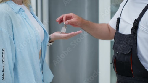 Close-up view of a professional construction worker giving the keys to a new home to the female owner, concluding the transaction with a grateful handshake for the completed repair job