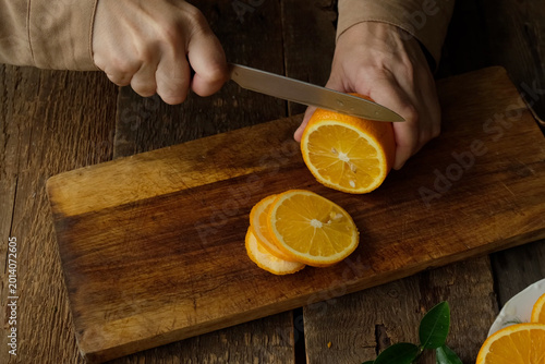 Woman slicing fresh oranges on wooden cutting board. Preparing citrus fruits for mulled wine or lemonade