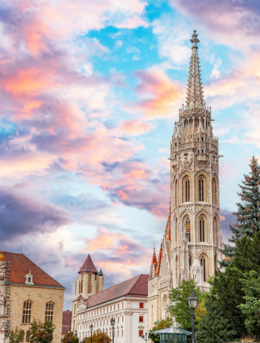 Ornate Gothic spire of Matthias Church in Budapest under a dramatic sunset sky with colorful clouds.