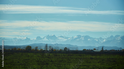 Early morning in autumn. In the distance, a settlement and the high mountains of the Caucasus