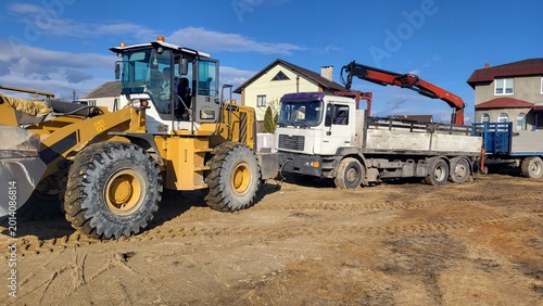 Yellow wheel loader and a white truck on a gravel construction lot, industrial building equipment, site management.