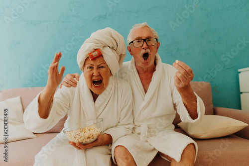Bild auf Leinwand Happy senior couple watching TV and eating popcorn.