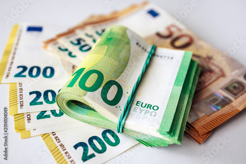 Close-up of a stack of euro banknotes with a rolled 100 euro bill placed on neatly arranged various euro currency notes on a flat surface. Concept finance, savings and money management.
