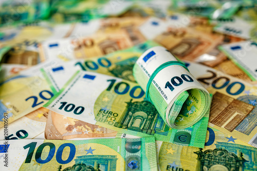 Detailed view of rolled 100 euro banknotes held together with a rubber band placed on mixed euro currency background. Concept banking, money management and economy.
