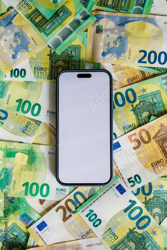 Smartphone with empty screen on euro banknotes arranged as background. Concept money app advertising and banking concept.
