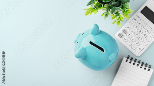 Top view of blue piggy bank with calculator and spiral notebook on blue background, finance planning, personal savings, and budgeting