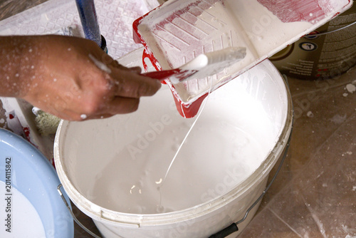 Tableau sur toile Person Cleaning Paint Tray with Brush Above Bucket of White Paint During Home Re