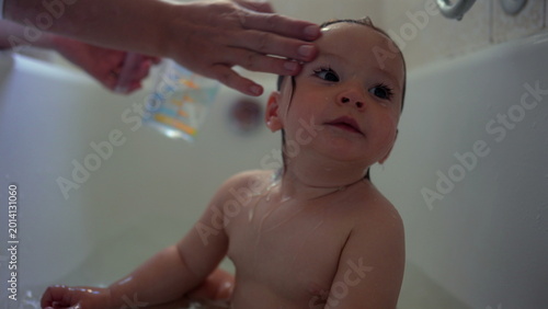 Photos Baby sitting in bathtub looking up with soft curious expression while water tric