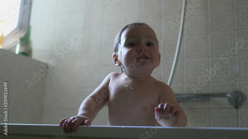 Bild auf Leinwand Baby standing in bathtub with water on skin, looking forward with calm alert exp