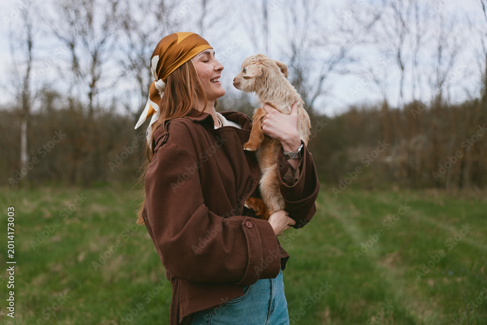 Fototapeta premium A joyful woman outdoors holds a fluffy animal close, smiling as they share a tender moment in a grassy field. A lifestyle portrait conveying warmth, connection, and affection between human and pet.