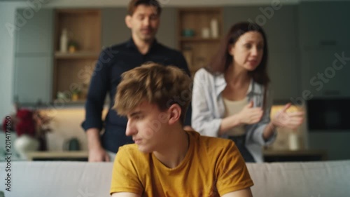 Unhappy teen boy listening to annoyed parents scolding him, emotional stress