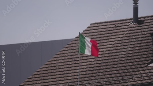 Italian flag waving with pitch roof in the background on a sunny spring day. Video shot May 8th, 2026, Zurich Rümlang, Switzerland.