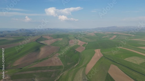 Rolling hills with a patchwork of green and brown fields under a bright sky.