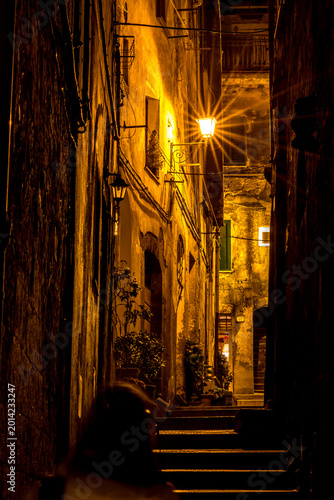 Diffraction view of street at night with person walking down the street, Sovana, Tuscany, Italy, long exposure motion blur
